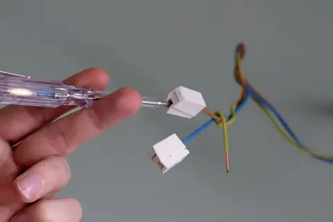 Hand prüft Kabel mit Schraubendreher, um eine Lampe anzuklemmen.