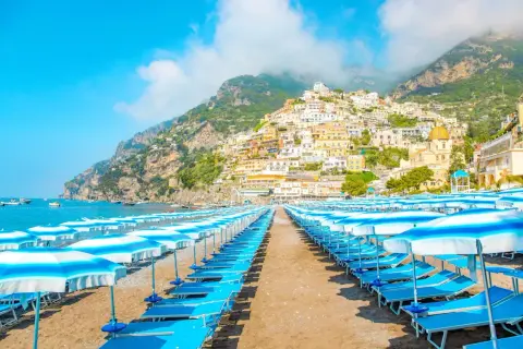 Rzędy leżaków i parasoli na plaży w Positano. W tle malownicze, kolorowe domy wznoszące się na zboczu góry. Idealne miejsce, by zobaczyć piękno Amalfi.