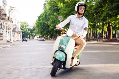 Mężczyzna w kasku i okularach jedzie stylowym, zielono-białym motorowerem na dowód osobisty po brukowanej ulicy.