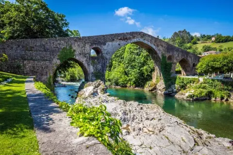 El histórico puente de Cangas de Onís cruza un río de aguas cristalinas rodeado de exuberante vegetación.