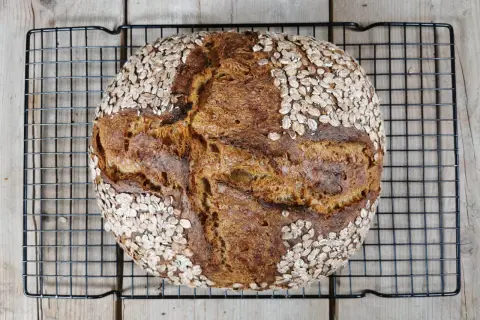 Ein rustikales Porridge Brot mit Haferflockenkruste, das auf einem Gitterrost abkühlt.