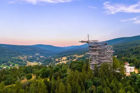 Metalowa konstrukcja sky walk wznosi się na znaczną wysokość nad zalesionymi wzgórzami, oferując zapierające dech w piersiach widoki.