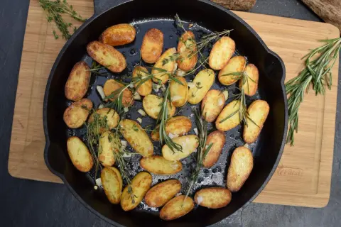 Goldbraune rosmarin kartoffeln mit Knoblauch und Kräutern in einer Gusseisenpfanne, bereit zum Servieren.
