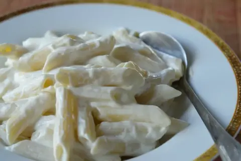 Penne z kremowym twarogiem na słodko, podane na talerzu z łyżką. Pyszne danie, które z pewnością zadowoli każdego.