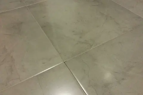 Detalle de la colocación de cerámica gris en un suelo, mostrando las juntas finas y el acabado mate.