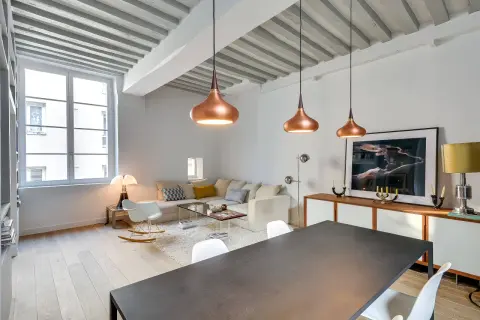 Lámparas colgantes de cobre y un diseño moderno reflejan las **últimas tendencias iluminación salones**. Un sofá blanco y una mesa de comedor completan el espacio.