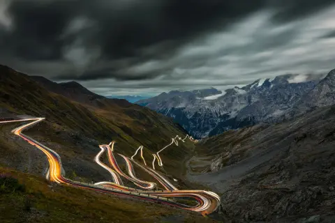 Ślady świateł samochodów wiją się serpentynami na stromych zboczach górskich, tworząc świetlisty szlak na przełęczy Stelvio.