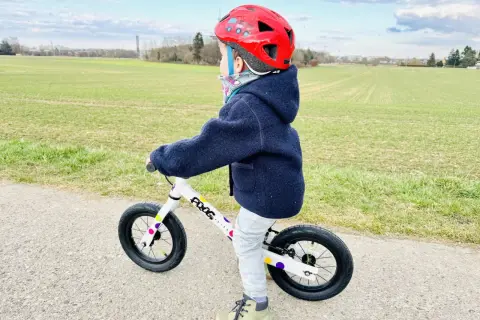 Kind mit rotem Helm übt das laufrad fahren auf einem Feldweg.