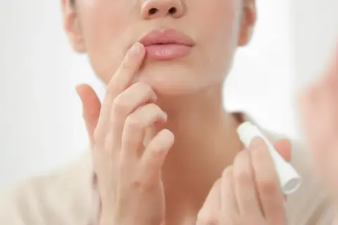Mujer aplicándose bálsamo labial para el cuidado de labios.
