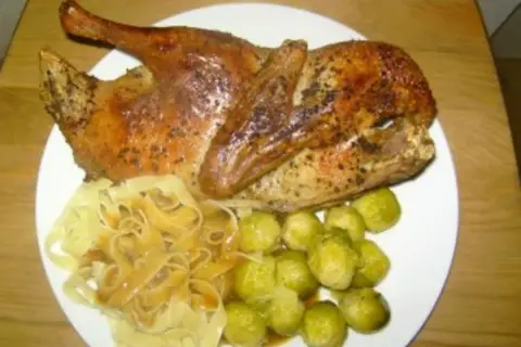 Halbe Ente braten, goldbraun und knusprig, serviert mit Bandnudeln und Rosenkohl. Ein Festmahl!