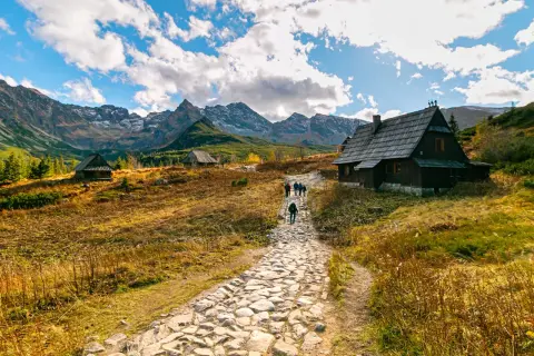 Kamienna ścieżka prowadzi do górskich chat. W oddali majestatyczne Tatry. To piękne zakopane atrakcje.