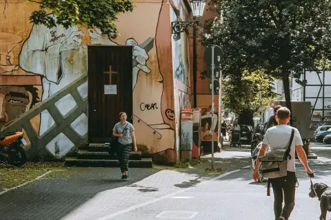 Ein Mann geht mit Hund durch eine Straße in Wuppertal, vorbei an einer Wand mit Graffiti.