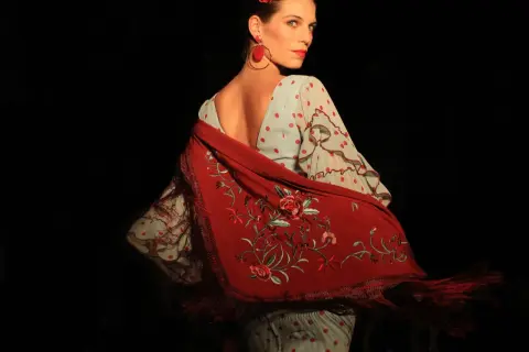 Mujer con traje de flamenca de lunares rojos y mantón bordado. Aprende como lavar un traje de flamenca para mantenerlo impecable.