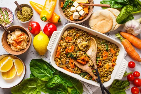 Un plat de lentilles aux légumes, une délicieuse recette végétarienne, servi avec du houmous, du pesto et des pains pita.