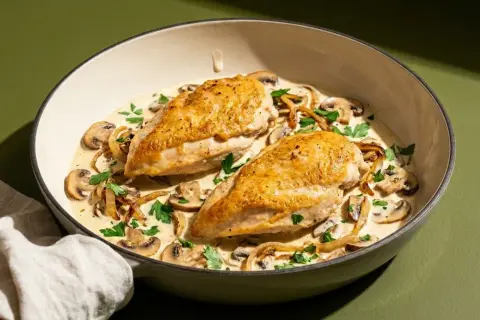 Zwei goldbraune Hähnchenbrustfilets, ein **supreme de poulet**, ruhen in cremiger Pilzsoße mit frischer Petersilie.
