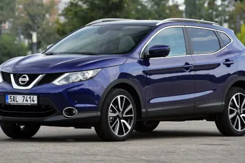 Granatowy Nissan Qashqai J11 z chromowanymi relingami dachowymi i felgami stoi na drodze.