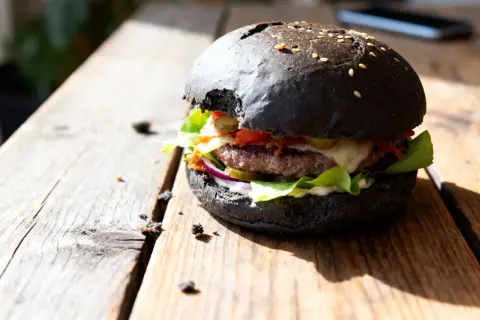 Burger maison avec pain noir, garni de salade, oignons rouges, cornichons, fromage et sauce.