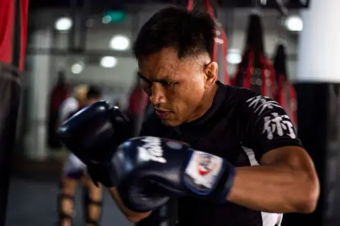 A boxer, sweat beading on his brow, trains intensely. This image shows why is boxing so tiring: constant movement, powerful strikes, and unwavering focus.
