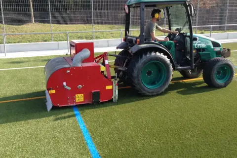 Traktor mit Anbaugerät reinigt Kunstrasen.