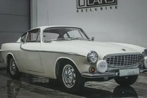 Vit Volvo P1800, en ikonisk bil som påminner om James Bond. Klassisk design med kromdetaljer och runda strålkastare.