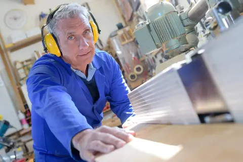 Ein Mann in Schutzkleidung arbeitet an einer Holzbearbeitungsmaschine. Seine Erfahrung im Handwerk spiegelt sich in seinen **altersteilzeit erfahrungsberichte** wider.