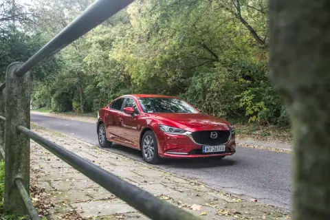 Czerwona Mazda 6 2.0 benzyna jedzie leśną drogą.