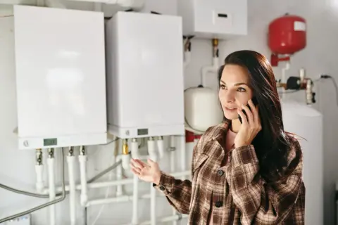 Kobieta rozmawia przez telefon, pytając jaki piec gazowy do mieszkania 70m2. W tle wiszą białe kotły gazowe.