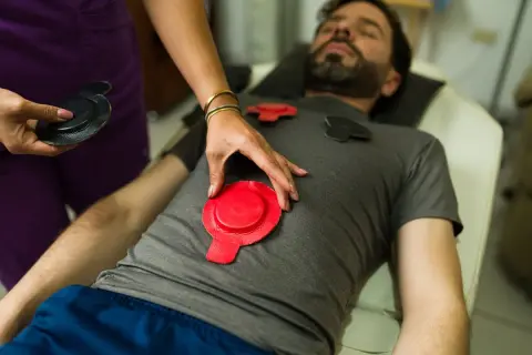 Un homme reçoit un traitement de magnétothérapie pour soulager son arthrose. Des électrodes rouges et noires sont placées sur son torse.