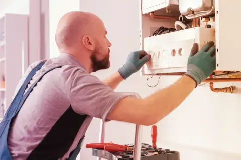 Tecnico con guanti verdi effettua la revisione caldaia in ritardo, regolando i comandi.