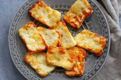 Gylla halloumi i airfryer, gyllene och krispiga bitar på en grå tallrik, kryddade med peppar.