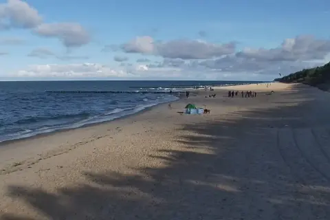 Piękny zachód słońca w Pobierowie. Ludzie spacerują po plaży, morze faluje, a niebo zdobią chmury.