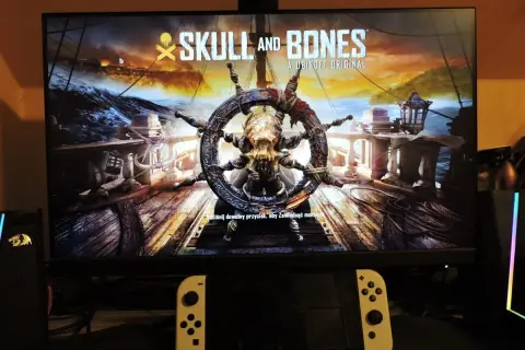 Logo gry "Skull and Bones" z kołem sterowym ozdobionym czaszką i kośćmi.