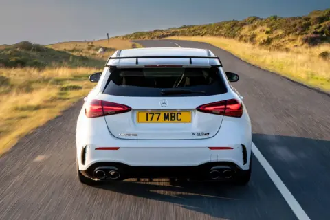 Biały Mercedes-AMG A45s pędzi po krętej drodze wśród wzgórz.