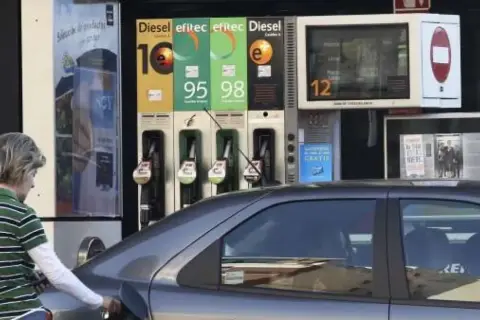 Persona repostando gasolina 95 o 98. El surtidor muestra los precios de los combustibles.