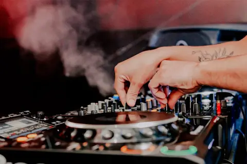 Mani esperte del dj sax mixano la musica, creando un'atmosfera vibrante con fumo e luci soffuse.