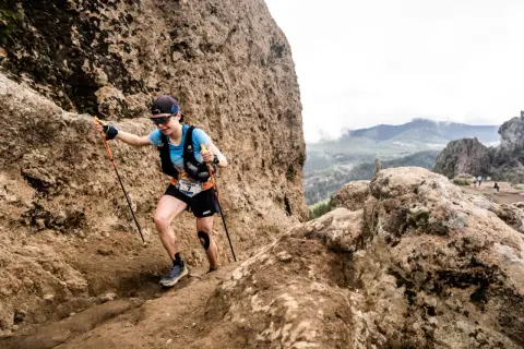 Katharina Hartmuth grimpe un sentier rocheux escarpé, bâtons en main, lors d'une course en montagne.