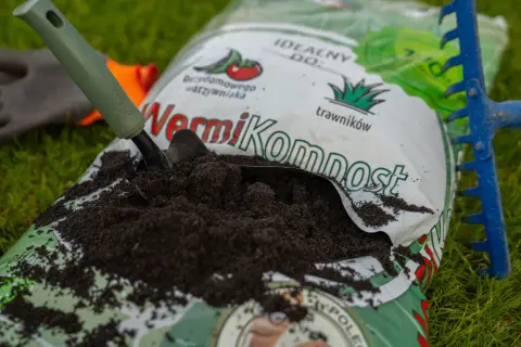 Worek z wermikompostem, łopatka i grabki na trawie. Idealny do warzywnika i trawników.