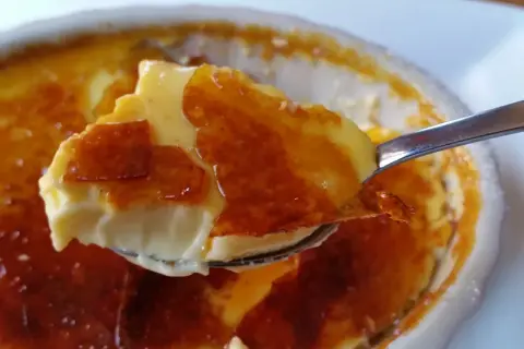 En sked lyfter en bit krämig creme brulee med knäckig yta.