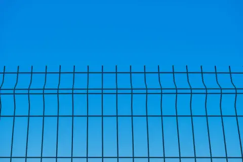 Siatka ogrodzeniowa na tle błękitnego nieba. Widać jej regularną strukturę i określoną wysokość.