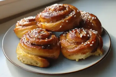Fem gyllene kanelbullar med pärlsocker på en blågrå tallrik. Perfekt för att grädda bullar varmluft eller inte.