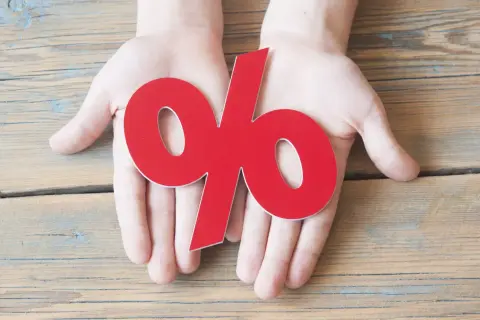 Dłonie trzymające czerwony symbol procentu. Dowiedz się, jak obliczyć odsetki ustawowe, aby zrozumieć finanse.