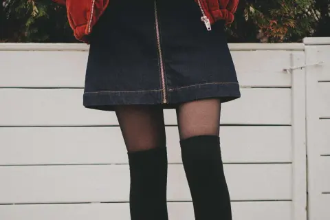 Stylowy outfit z dżinsową spódniczką, czarnymi zakolanówkami i pomarańczową kurtką.