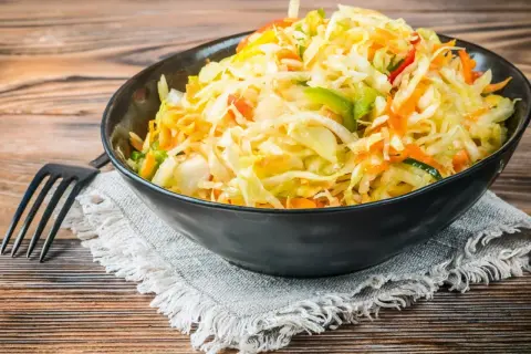 Kolorowa surówka z kiszonej kapusty inaczej, z dodatkiem marchewki, papryki i innych warzyw, podana w czarnej misce.