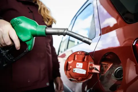 En person fyller på moms på bensin vid en röd bil. En grön bensinpump är i handen.