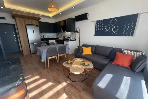 Nowoczesny salon z aneksem kuchennym, idealny na najem krótkoterminowy. Sofa, stolik kawowy, jadalnia i kuchnia.