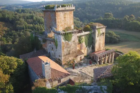 El **castillo de Pambre**, una fortaleza de piedra antigua, se alza entre bosques frondosos. Sus muros cubiertos de hiedra y tejados rojizos evocan historias de antaño.