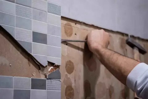 Persona usando un cincel para quitar juntas de azulejos viejos y dañados de una pared.