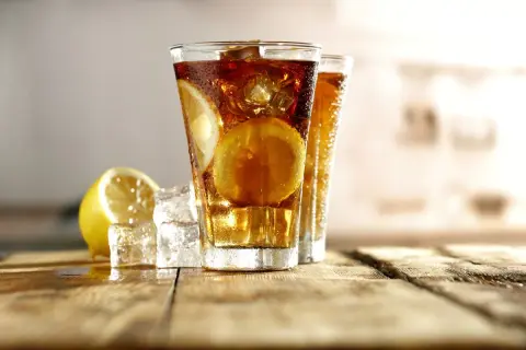 Dwa orzeźwiające drinki Long Island Ice Tea z plasterkami cytryny i kostkami lodu na drewnianym blacie.