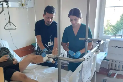 Lekarz i pielęgniarka w szpitalnej sali badają nogę pacjenta z aparatem zewnętrznym.