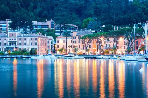 Serata a Toscolano Maderno: hotel illuminati, barche a vela e riflessi sull'acqua creano un'atmosfera magica.
